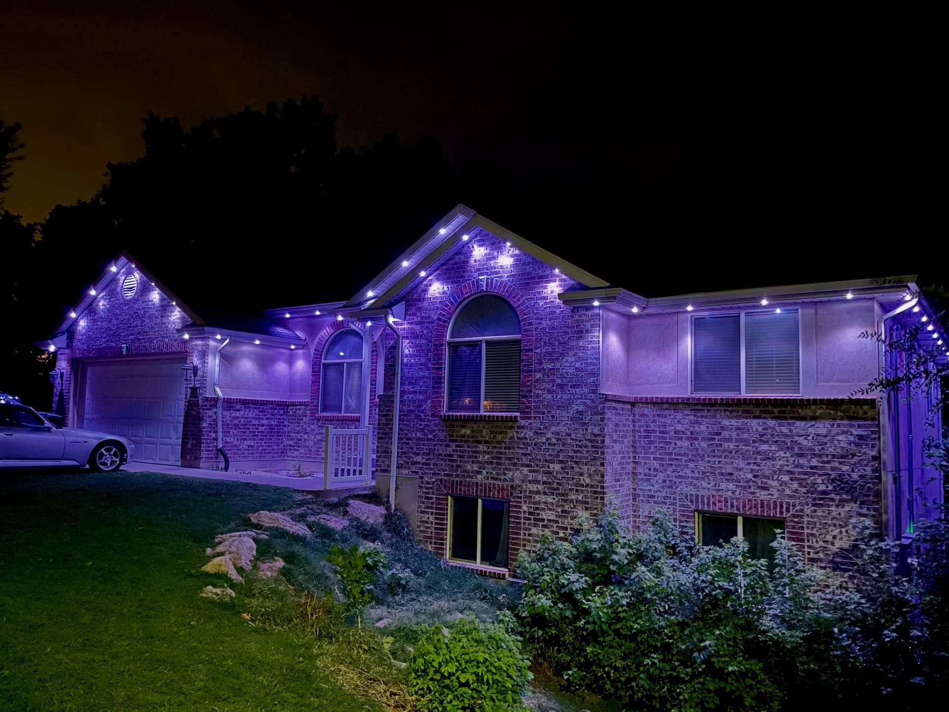 Brick home lit vivid purple with white eave accents at night