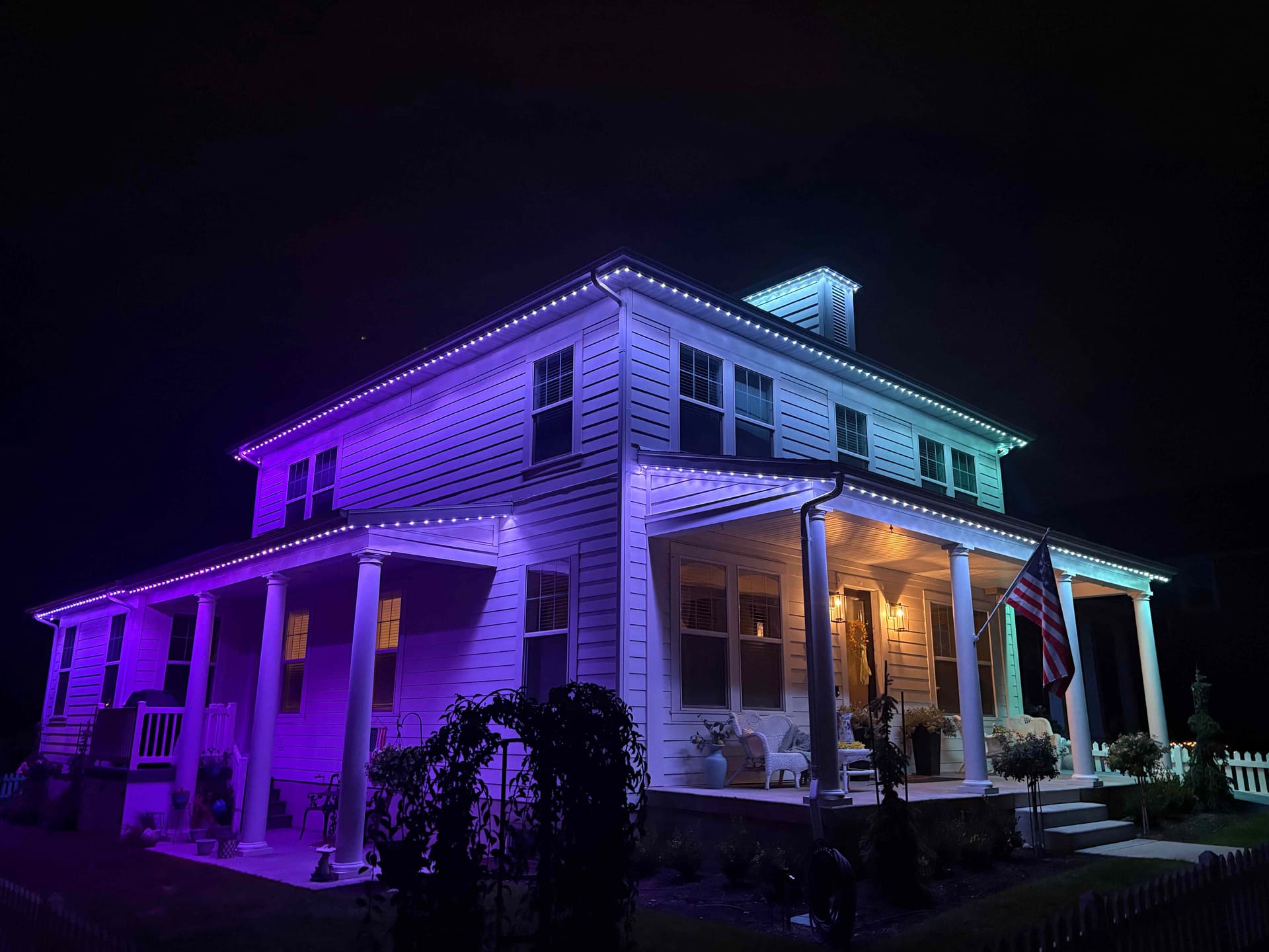White two-story home lit purple on one side and teal on the other