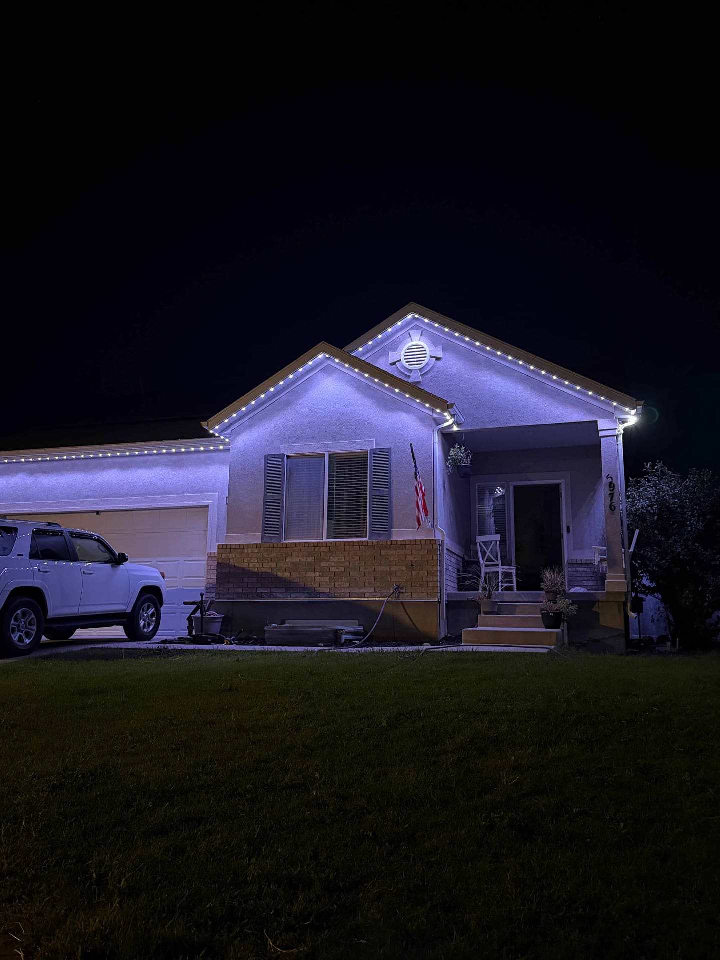 Stucco home with warm white roofline lighting and an American flag on the porch