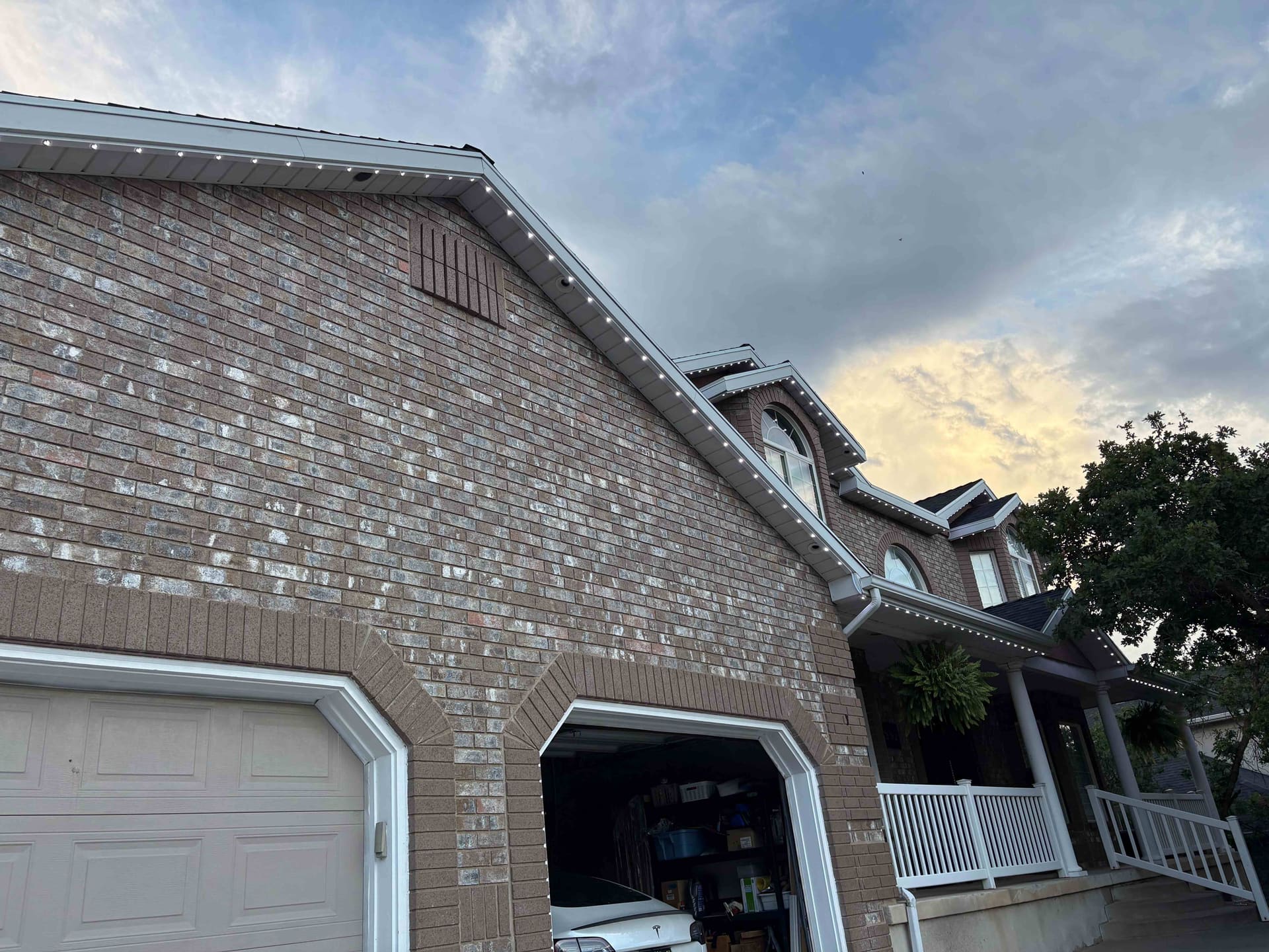 Close-up of a brick two-story home with clean warm white soffit lighting along the eaves