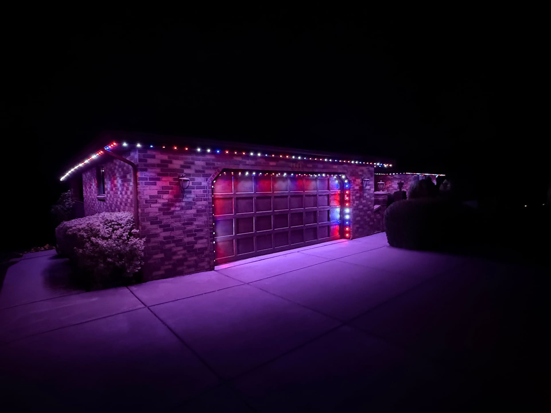 Brick garage lit red, white, and blue with a purple driveway wash