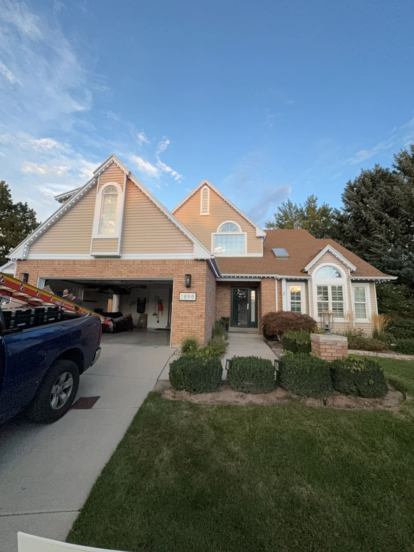 Two-story brick and beige-siding home with crisp warm white roofline and gable lighting at dusk